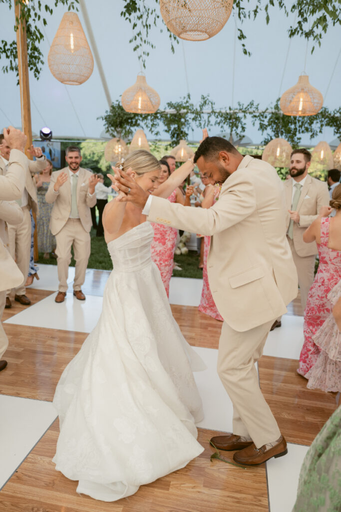 The bride and groom light up the dance floor, laughing and moving in sync surrounded by cheering guests.