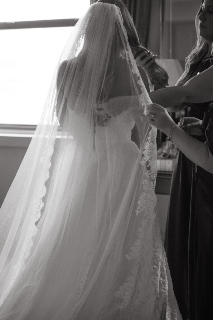 Bridesmaids adjust the bride’s veil in soft light—tender Moments You Won’t See on Your Wedding Day.