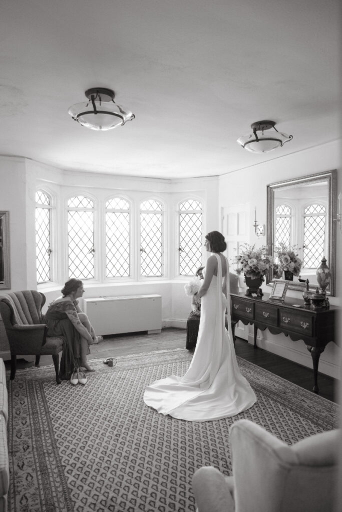 Bride stands in soft morning light while loved ones look on—intimate Moments You Won’t See on Your Wedding Day.