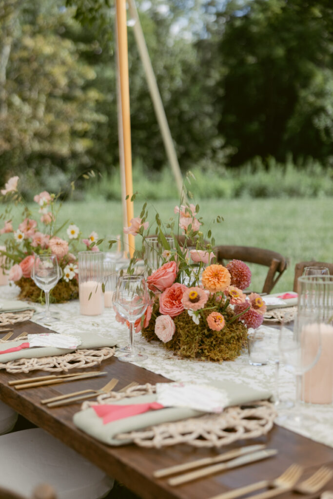 Outdoor wedding table with colorful floral centerpieces, candles, and elegant place settings on lace linens.