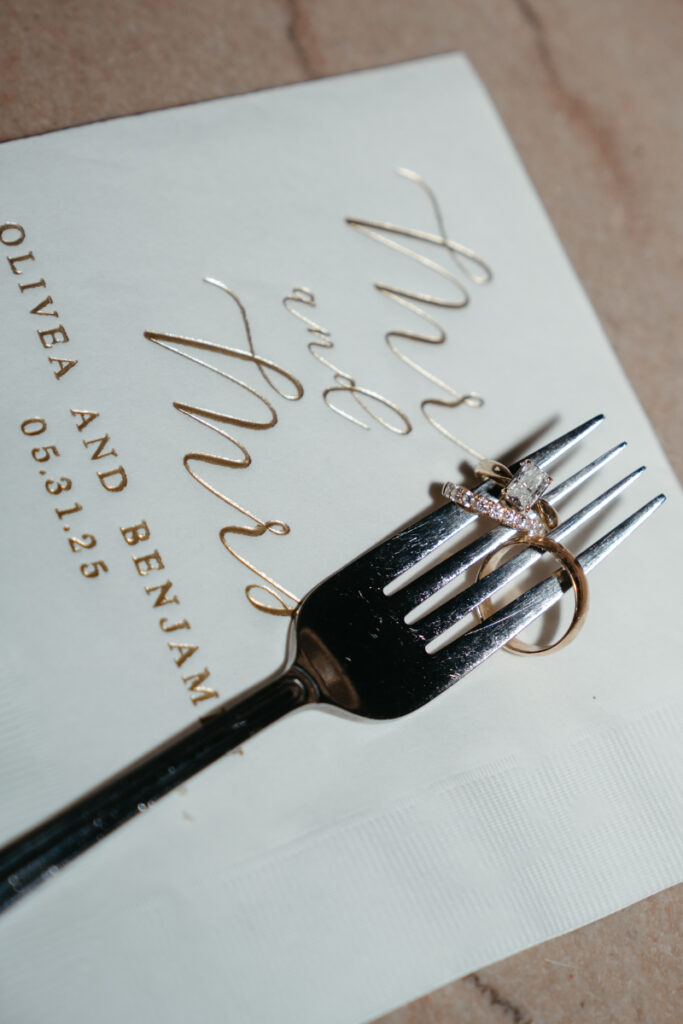 Wedding rings styled on a fork over elegant stationery—perfect detail for couples who just got engaged.