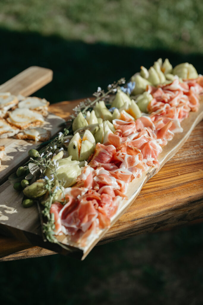 Charcuterie board with prosciutto, fresh figs, and herbs displayed on a rustic wooden table.