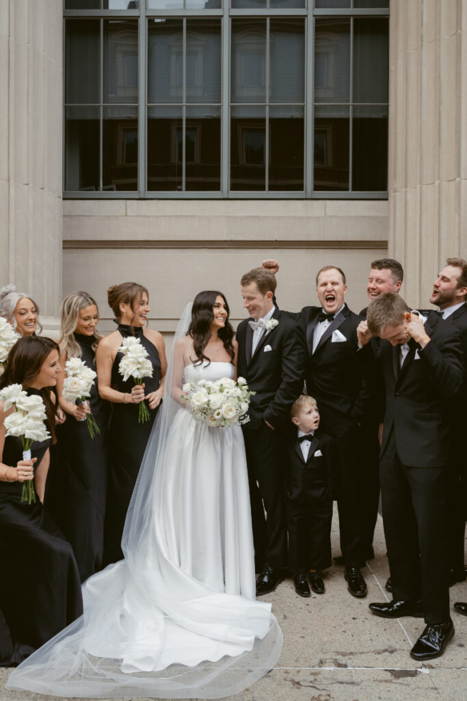 Wedding party celebrates outdoors with the bride and groom, dressed in classic black and white attire.