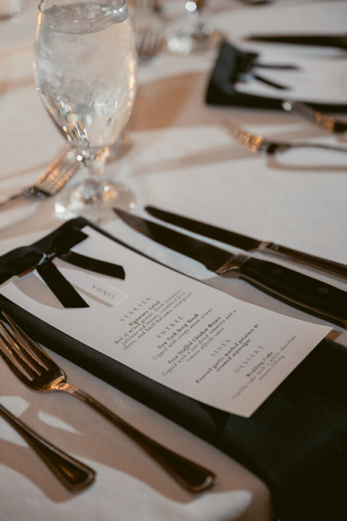 Elegant black-tie menu tucked into a napkin for a cozy Christmas wedding dinner table setting.