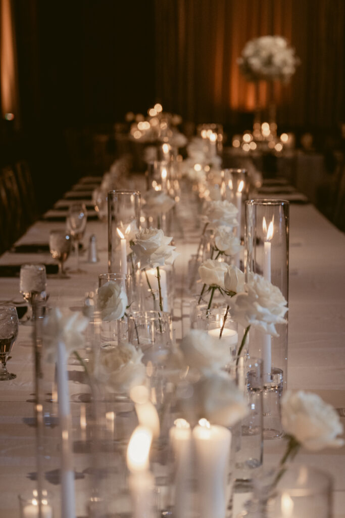 A long reception table lined with white roses and candles for a cozy Christmas wedding.