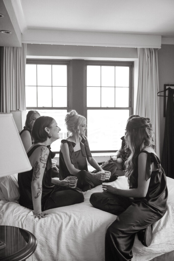 Bridesmaids in matching pajamas sitting on bed, sharing drinks before cozy Christmas wedding morning.