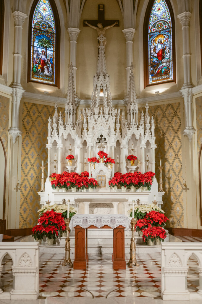 Stunning church altar adorned with red poinsettias and glowing stained glass windows.