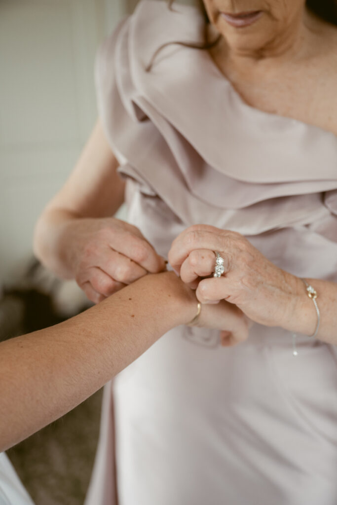 Mother of the bride helping with bracelet before cozy Christmas wedding, wearing elegant mauve dress.