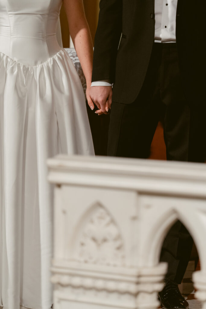 close up of a bride and groom holding hands during their wedding ceremony at a church
