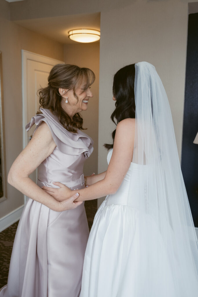 Bride and mother sharing a joyful moment before cozy Christmas wedding, holding hands and smiling.