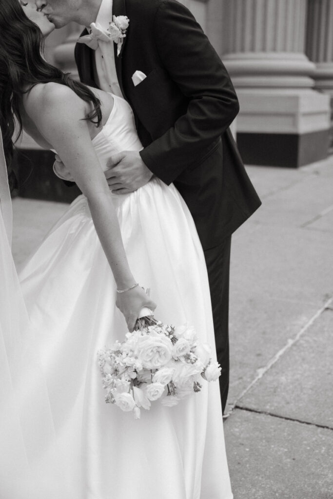 Groom dips the bride for a kiss while she holds her white rose bouquet.