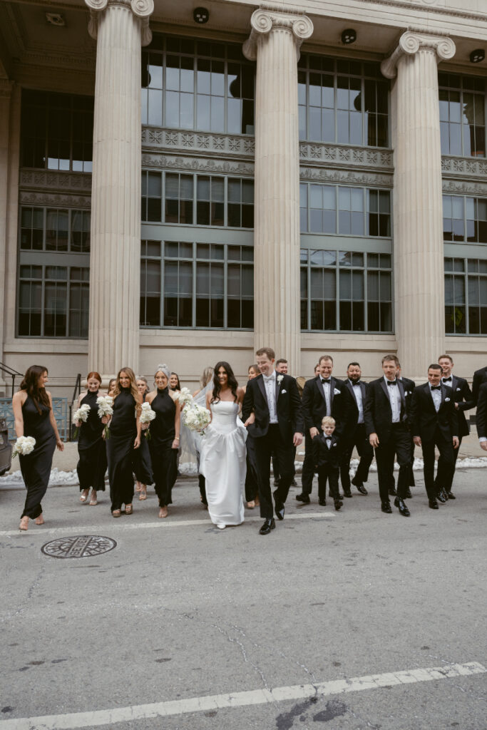 Bride and groom lead their wedding party across the street in a joyful, city wedding moment.