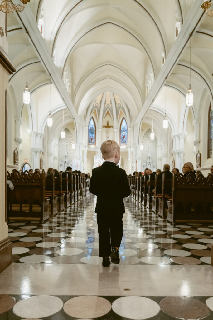 young boy ring bearer walking down the aisle at a church Christmas wedding