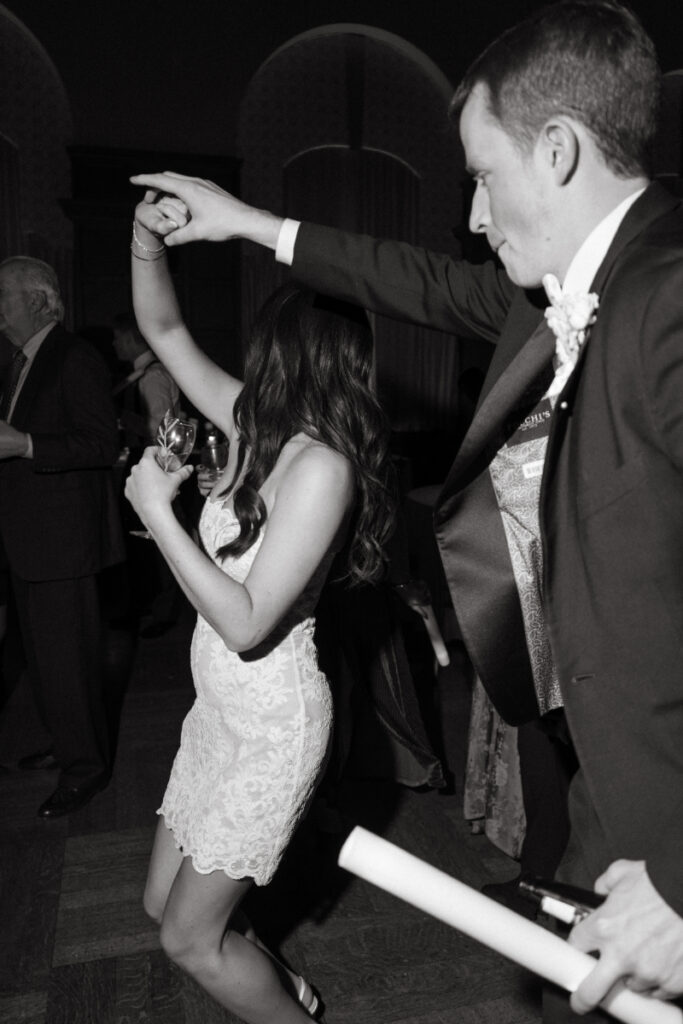 The groom twirls the bride on the dance floor as she smiles, holding a drink.