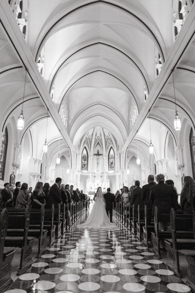 The bride walks down the aisle of a grand church during her cozy Christmas wedding ceremony.