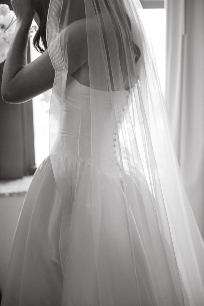 Bride in classic gown and veil stands near window during cozy Christmas wedding morning in Cincinnati.