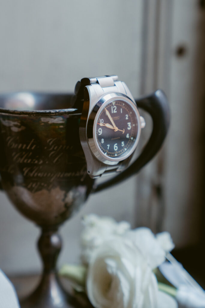 Groom’s watch displayed on vintage trophy with white rose details for cozy Christmas wedding.