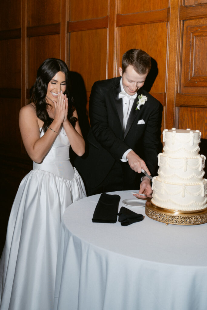 The groom cuts the cake as the bride reacts with joy during their winter wedding reception.
