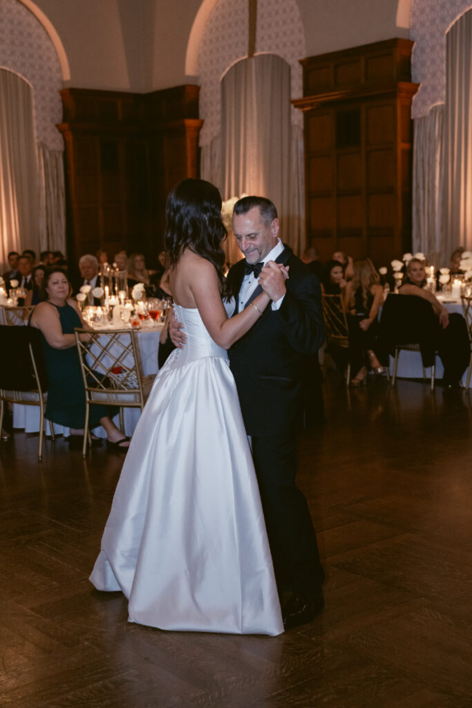 The father-daughter dance continues with smiles and laughter as guests look on warmly.