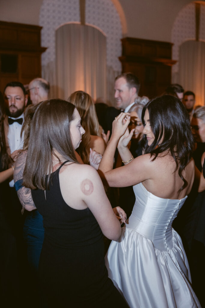 The bride dances joyfully with friends on the dance floor, celebrating the night with laughter and energy.