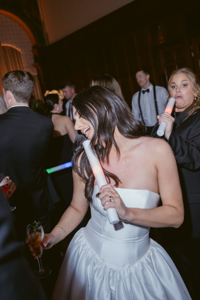 The bride dances with a big smile, holding champagne and surrounded by happy guests.