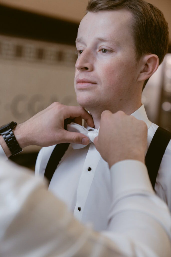 Groom getting his white bow tie adjusted while getting ready for his cozy Christmas wedding