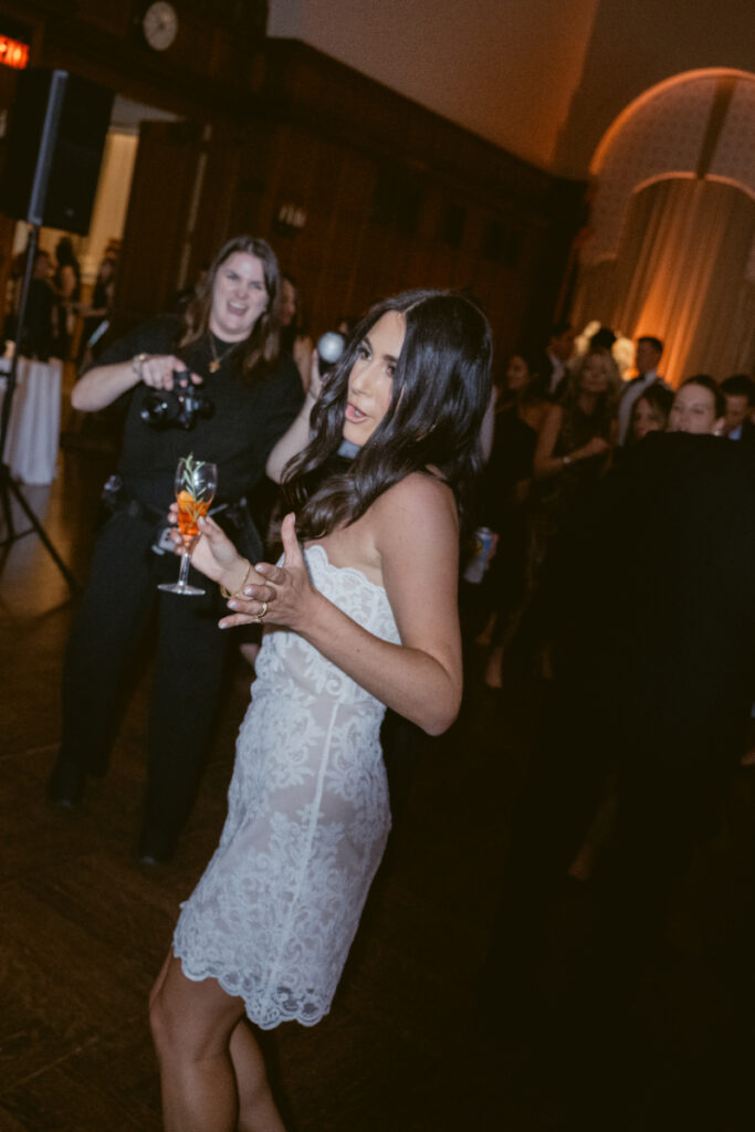 The bride enjoys the dance floor in a short lace dress, drink in hand.