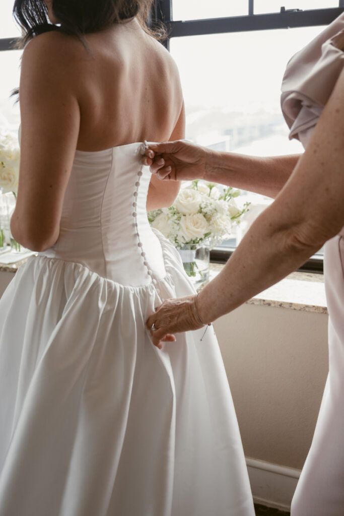 Bride’s gown being buttoned by her mother before cozy Christmas wedding, with roses in the background.