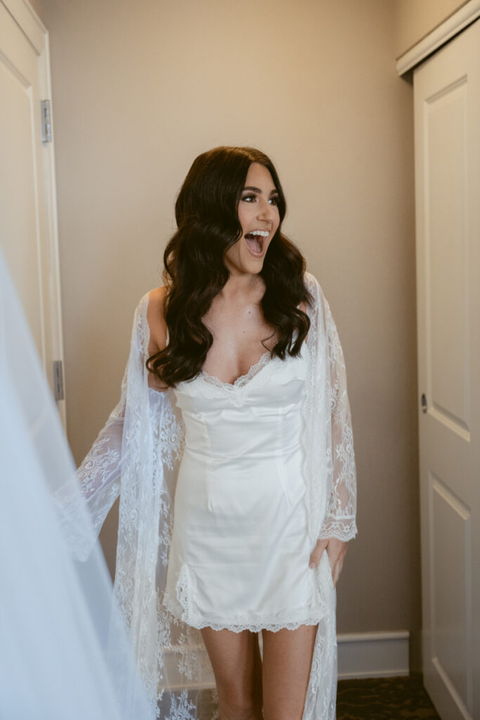Excited bride in satin robe during cozy Christmas wedding morning, smiling while getting ready.