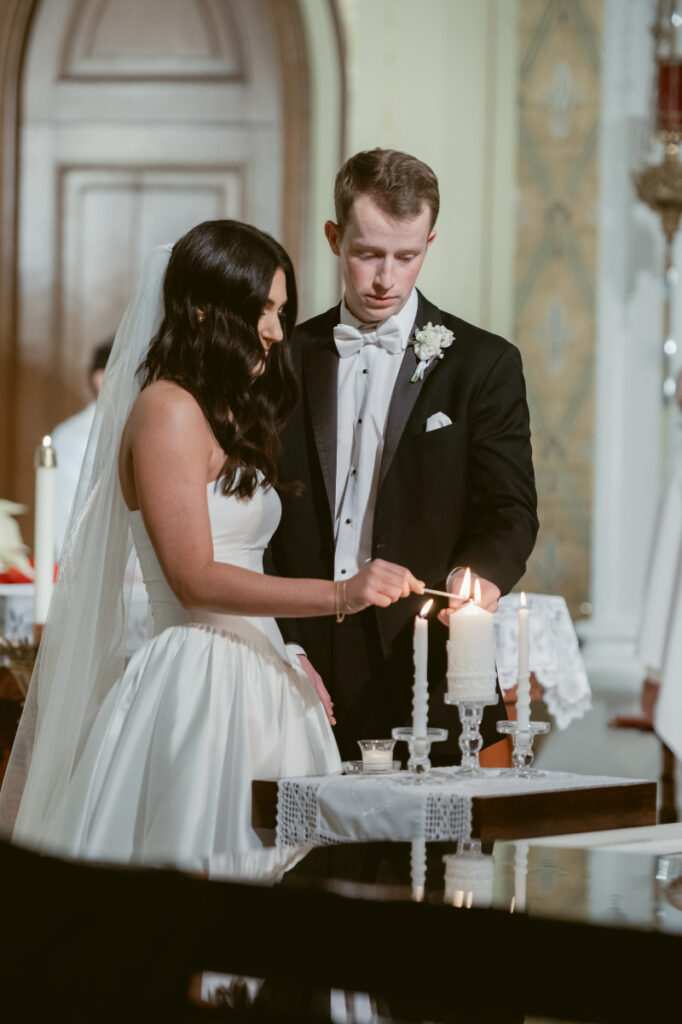 The bride and groom light a unity candle together during their cozy Christmas wedding ceremony.