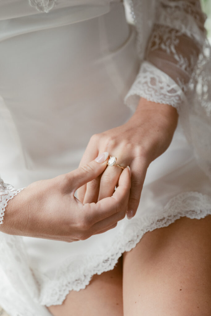 Bride adjusting engagement ring while getting ready for cozy Christmas wedding, wearing lace robe.