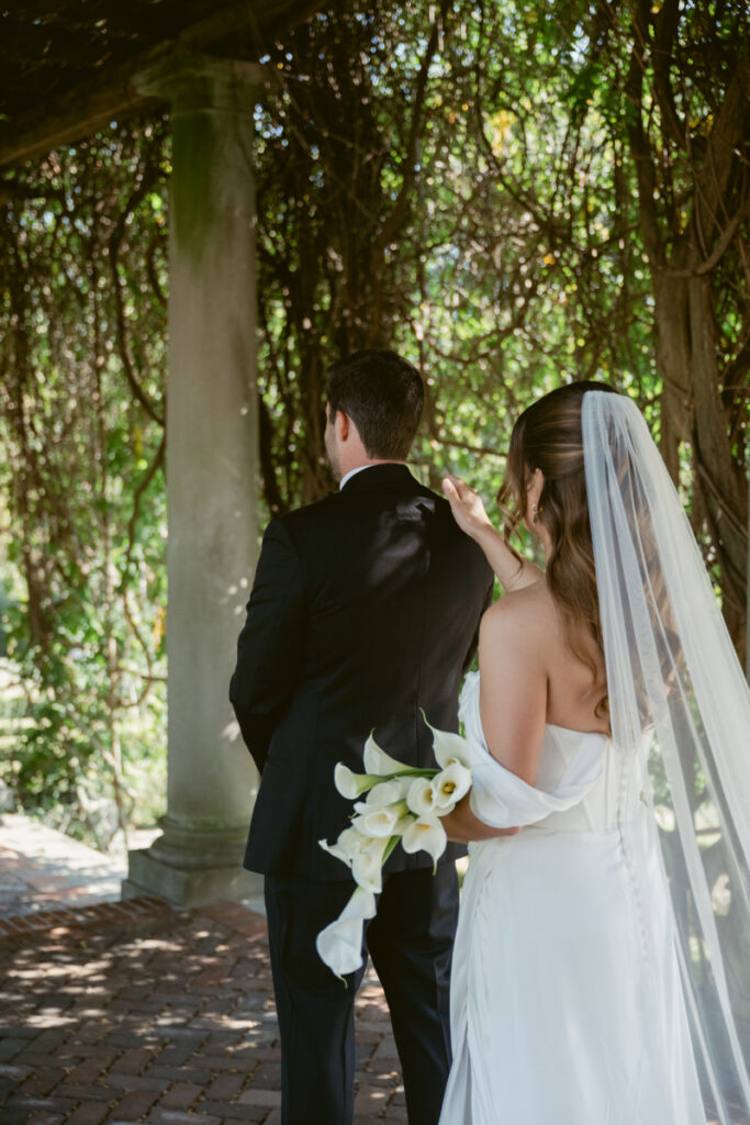 Bride and groom during emotional first look moment under greenery, bride holding white calla lilies.