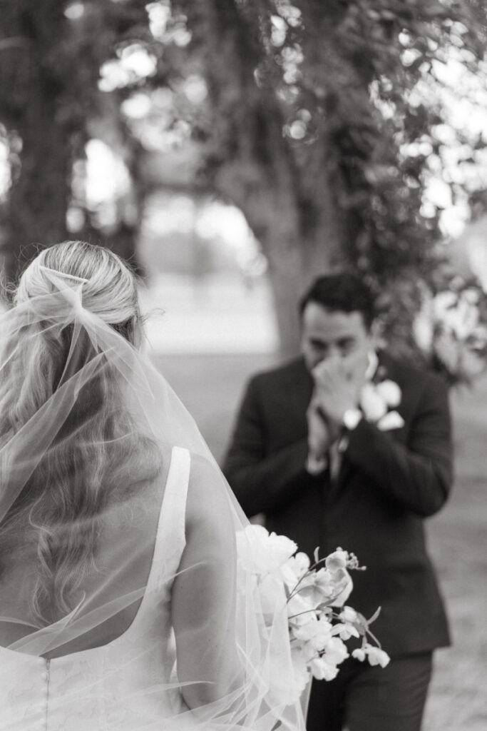 Groom reacts emotionally as bride approaches, captured in a black and white close-up moment.