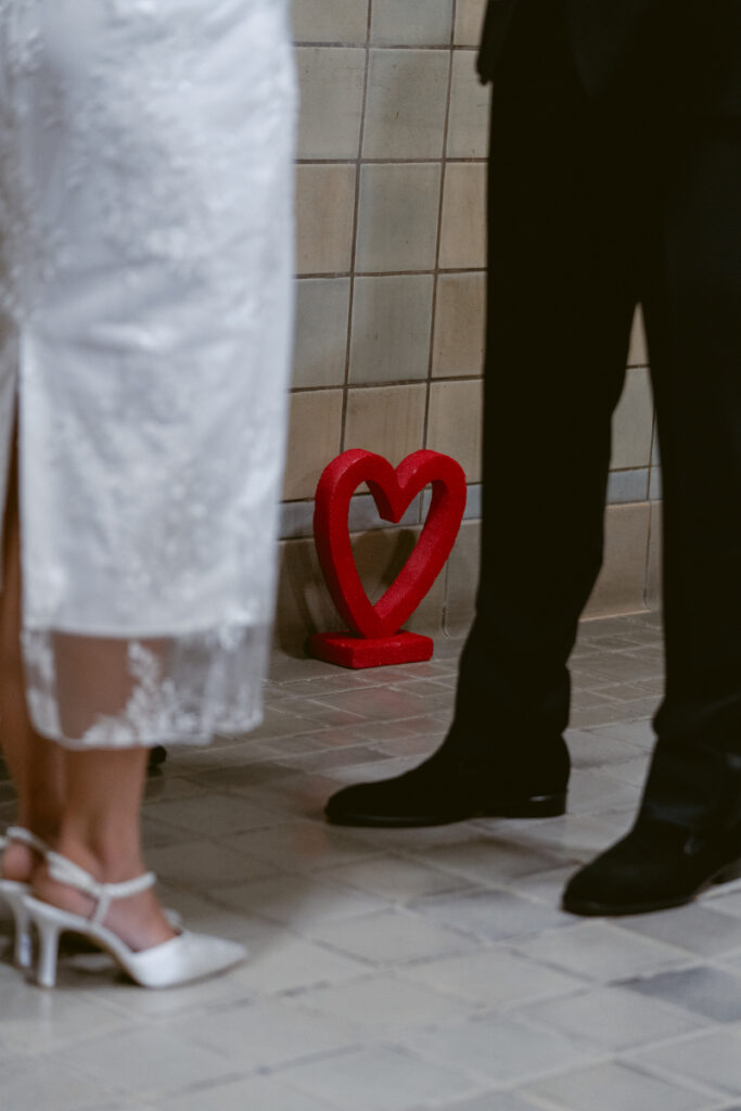 Bride and groom standing near red heart decor at Valentine’s Day wedding ceremony.