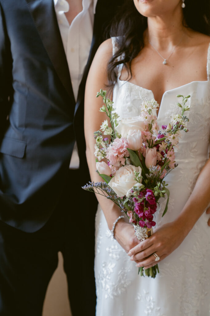 Bride holding pink bouquet with groom beside her at Valentine’s Day wedding.