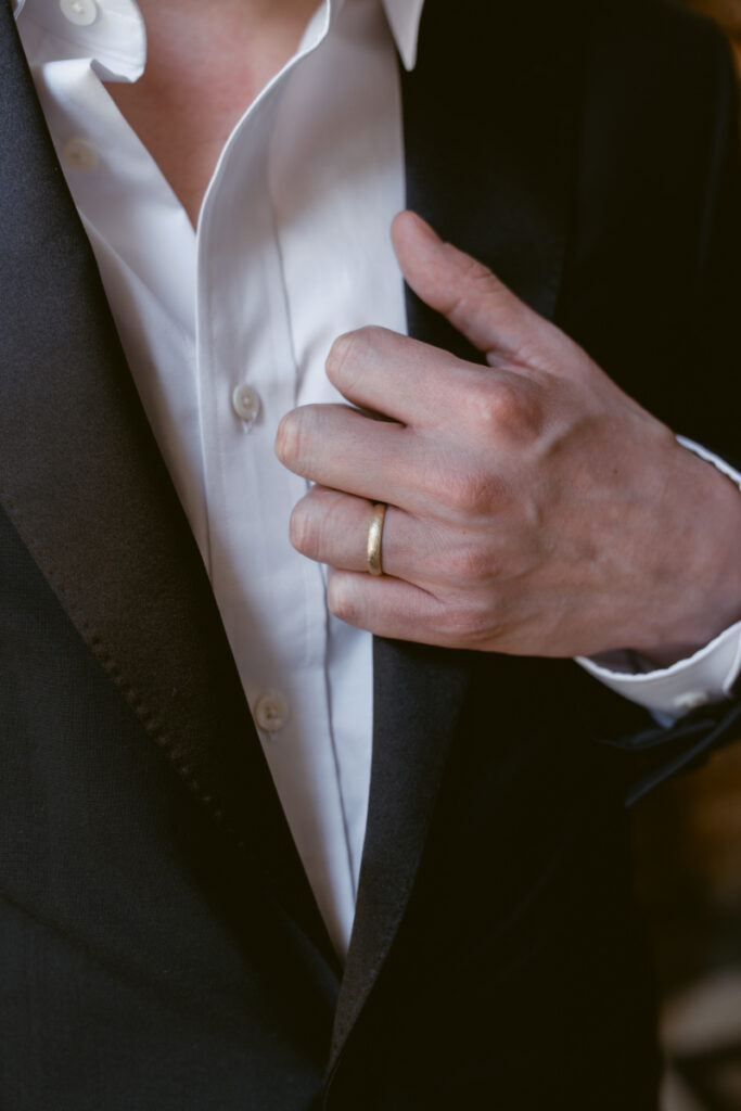 Groom adjusting jacket and showing wedding band during Valentine’s Day wedding.
