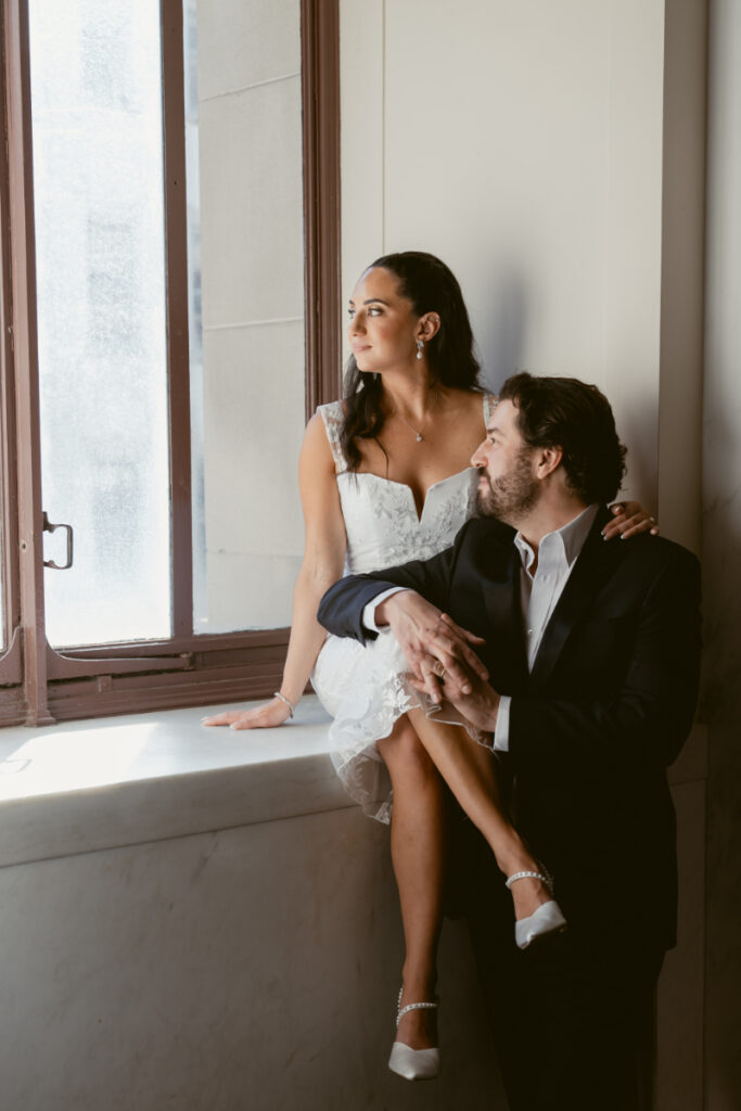 Bride and groom seated by window during intimate Valentine’s Day wedding portraits.