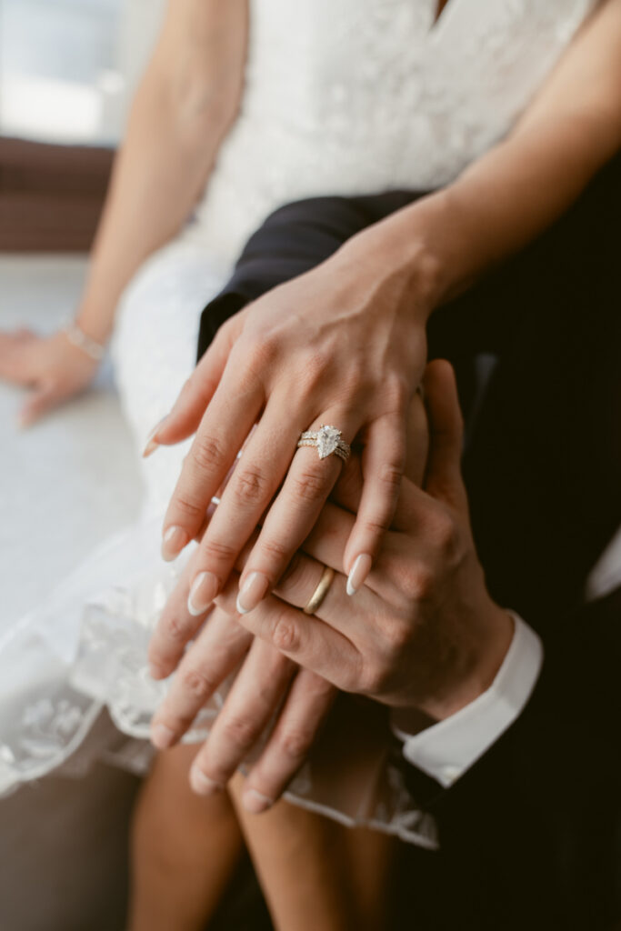 Bride’s engagement ring resting on groom’s hand at Valentine’s Day wedding.