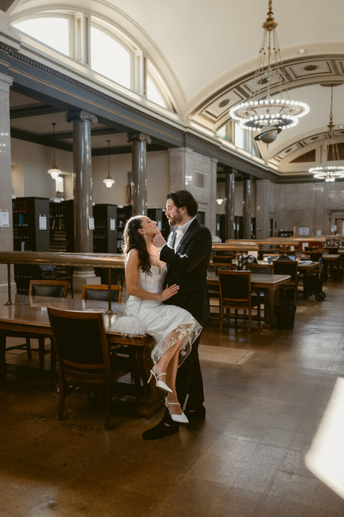 Bride sitting on table with groom during romantic Valentine’s Day wedding portraits.