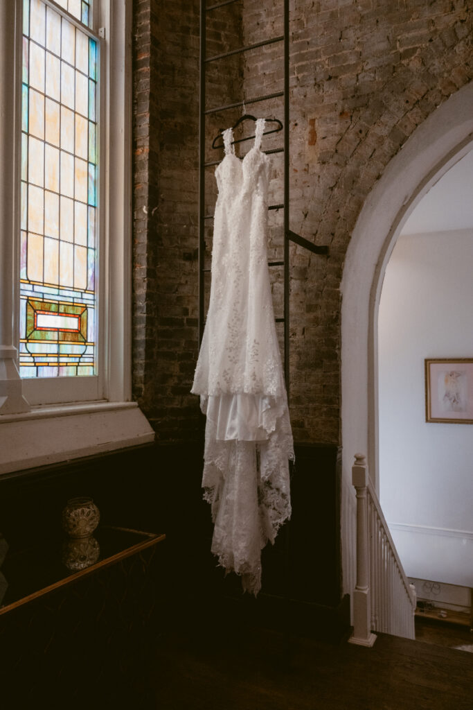 Wedding dress hanging by stained glass window inside historic venue.