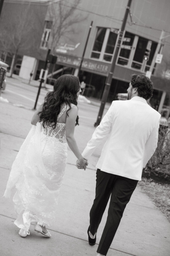 Bride and groom walking hand in hand through city street.