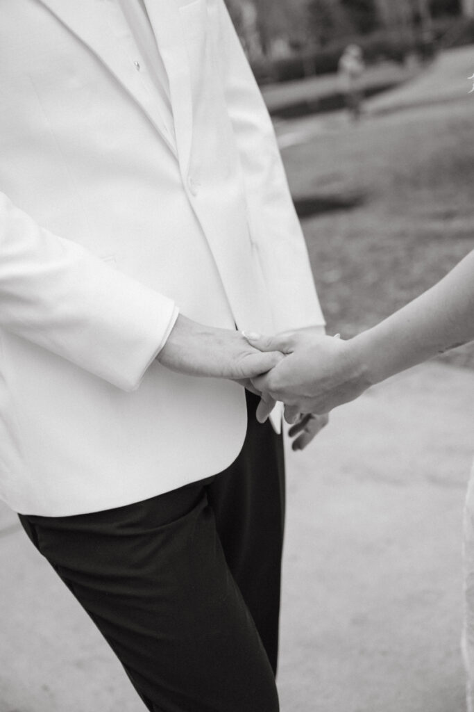 Black and white close up of couple holding hands outdoors.