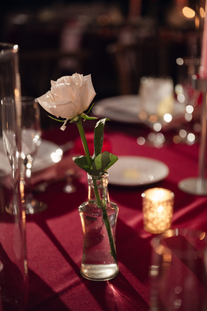 Single white rose in glass vase on red reception table.