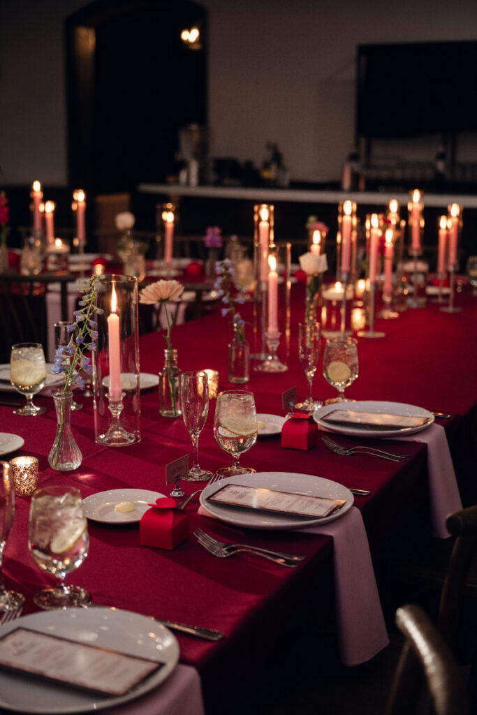 Long reception table with red linens and tall candle centerpieces.