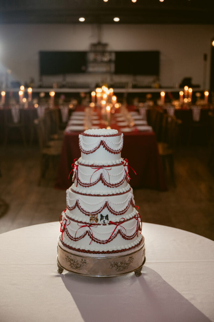 Four tier white wedding cake with red ribbon details at reception.