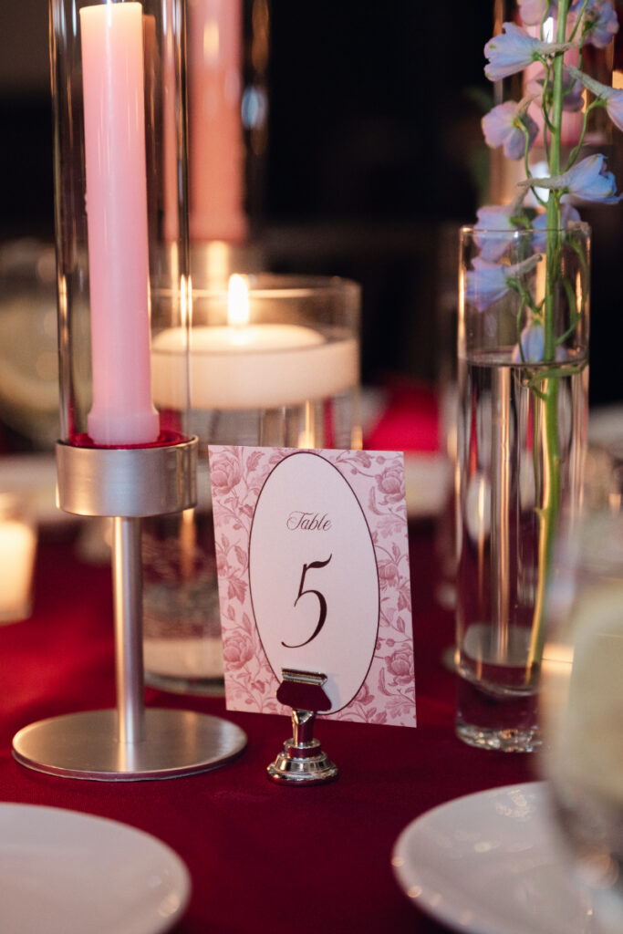 Table number five card beside pink candle on red table setting.