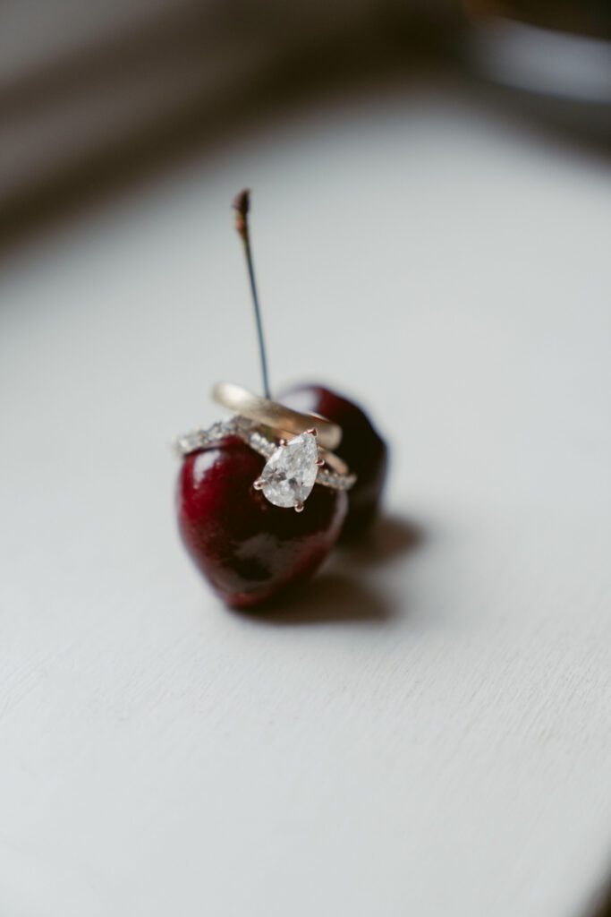 Engagement ring balanced on cherry in styled detail photo.