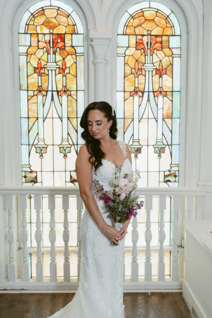 Bride holding bouquet in front of stained glass windows.