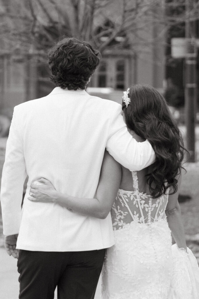 Black and white photo of bride and groom walking arm in arm from behind.