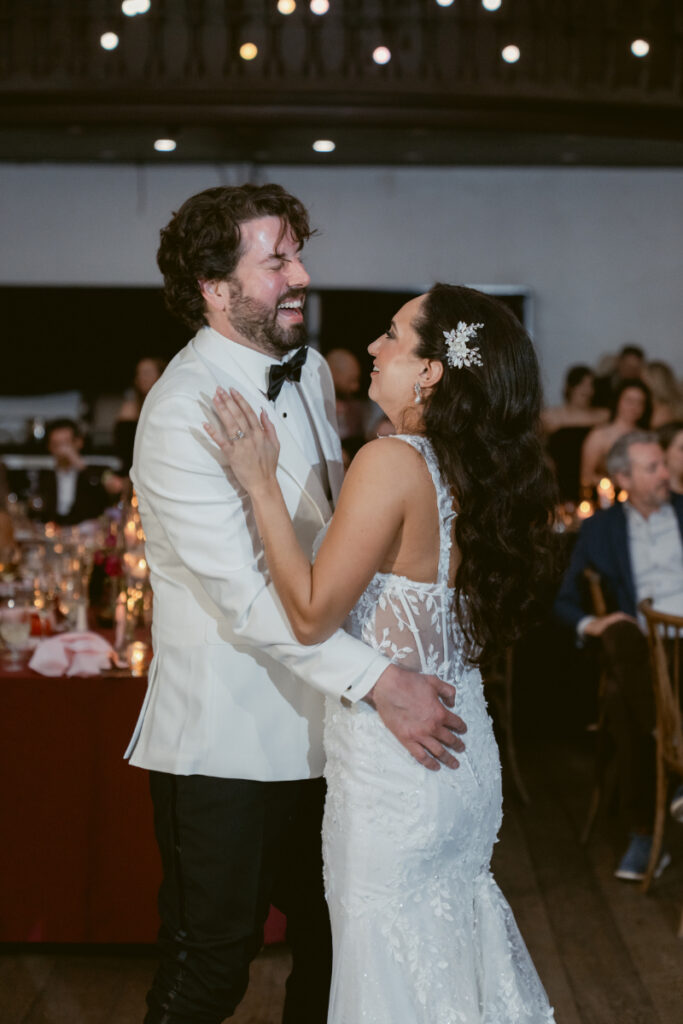 Bride and groom laughing while dancing at evening reception.